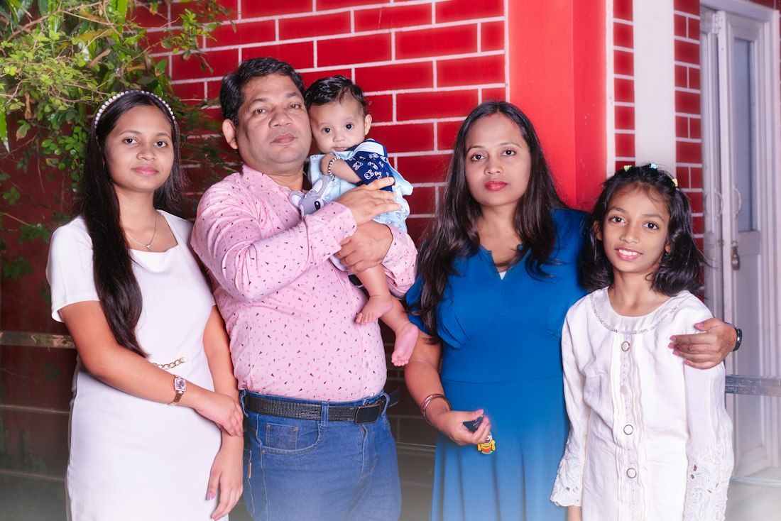 A smiling family of five standing against a red wall