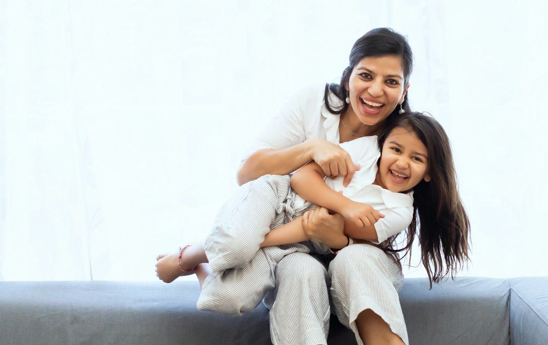 A mother and her young daughter laughing together on a sofa