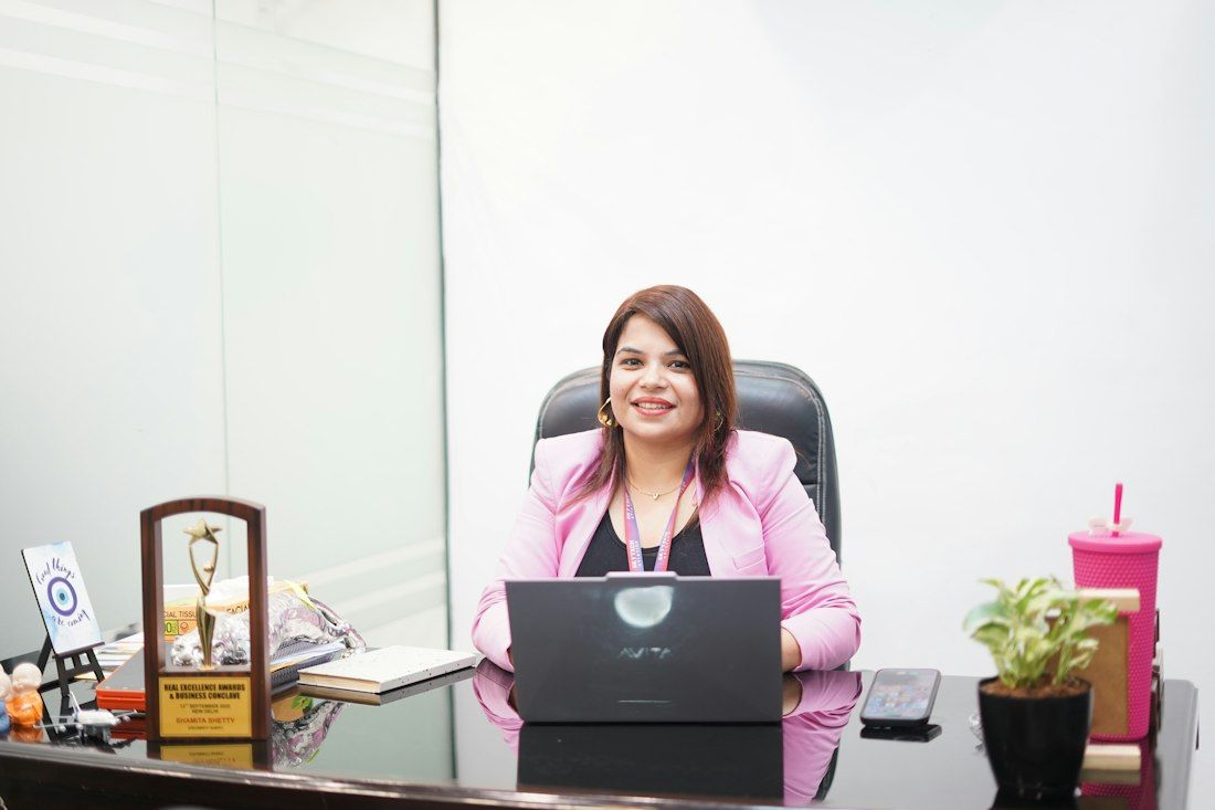 Smiling professional woman in a pink blazer at her office desk