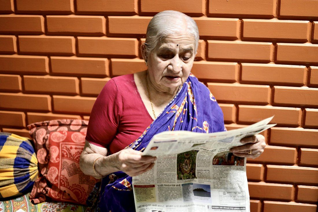 An elderly woman in a sari reading the morning newspaper