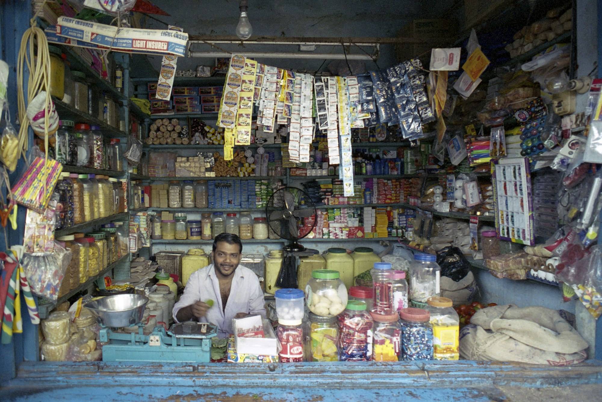 Smiling shopkeeper behind the counter of a well-stocked general store