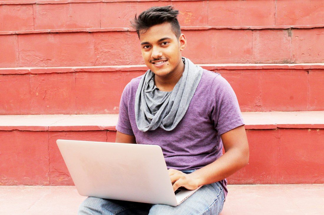 A smiling student with a laptop sitting on red steps