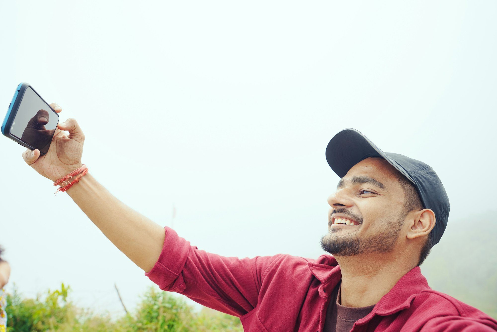Young man in a red shirt and cap taking a selfie under a bright sky