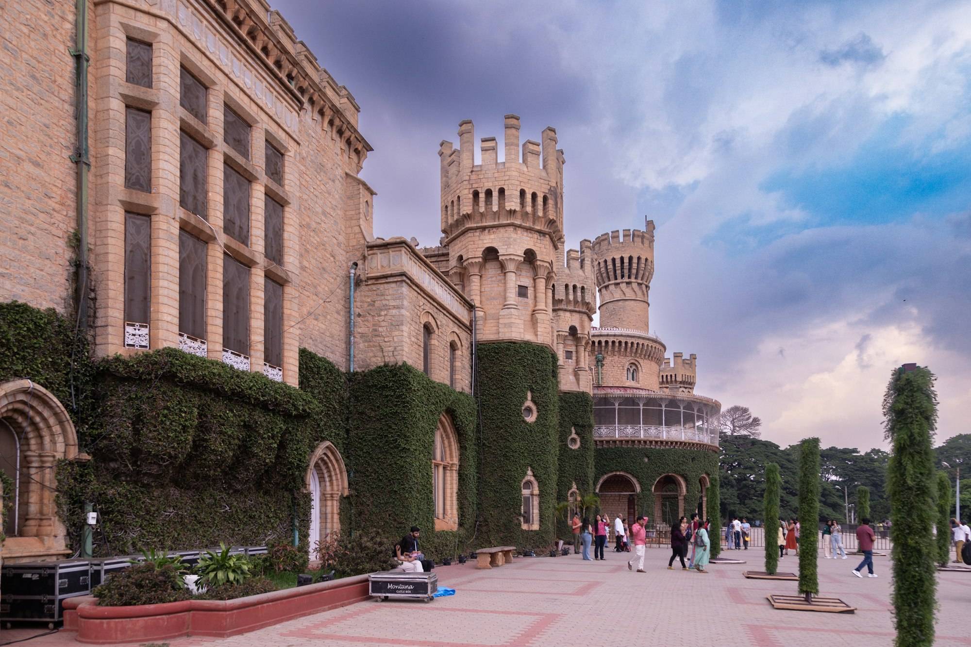 Visitors in the forecourt of Bangalore Palace under a dramatic sky