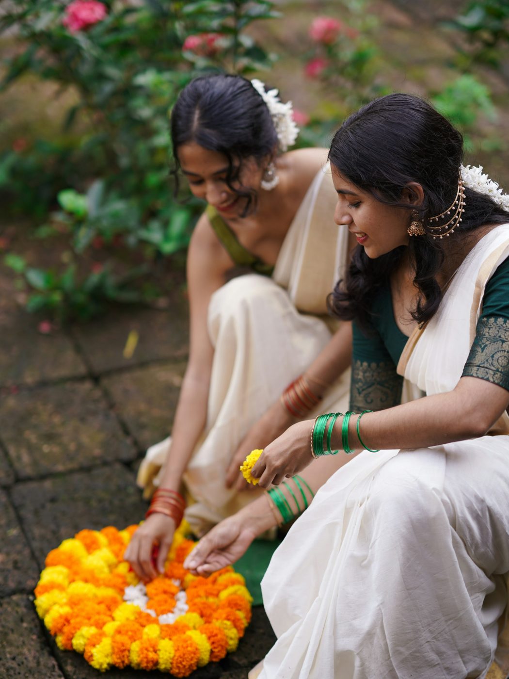 Two women arranging a marigold rangoli